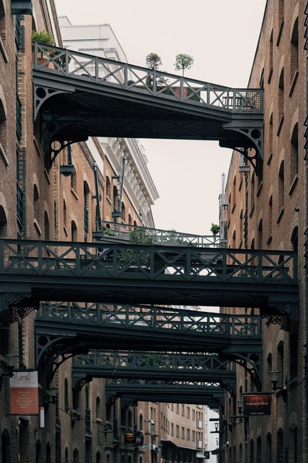 A white moving van with an open cargo area parked on a paved street beneath an elevated railway bridge with green and white trains passing overhead. The van is positioned near a building entrance or l